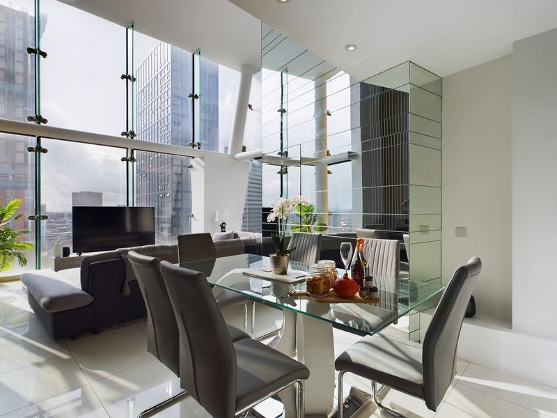 Modern living room with floor-to-ceiling windows, glass dining table, dark furniture and city views