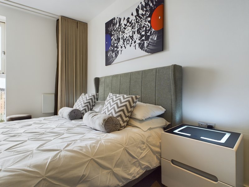 Modern bedroom with gray upholstered headboard, patterned bedding, and abstract wall art