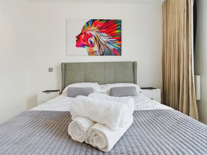 Modern bedroom with grey upholstered headboard, white pillows, folded towels on bed