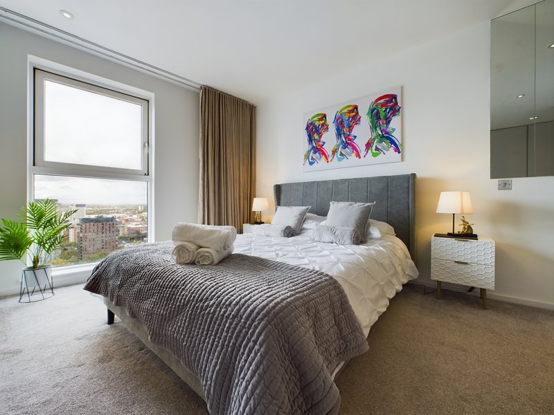 Modern bedroom with double bed, grey headboard, nightstands, large window with city view