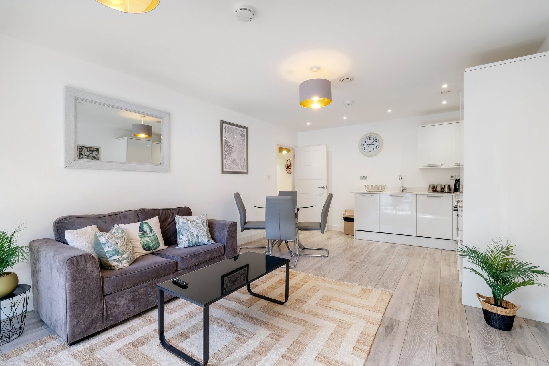 Open-plan living room with grey sofa, dining table, white kitchen, and wooden flooring