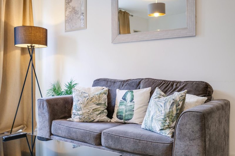 Modern living room with gray upholstered sofa, decorative cushions, floor lamp and wall mirror