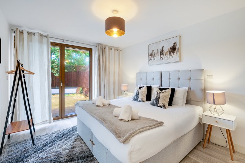 Bright modern bedroom with double bed, upholstered headboard, wooden floor and patio doors