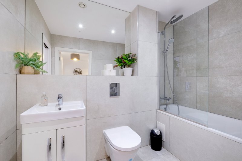 Modern bathroom with white vanity, mirror, potted plants, toilet and bathtub with shower screen