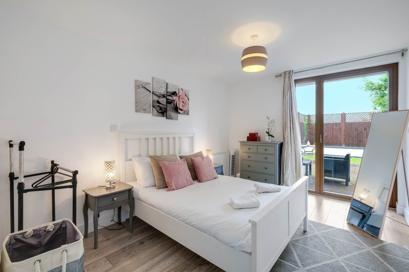 Bright bedroom with white bed, pink pillows, wooden floor and glass patio doors
