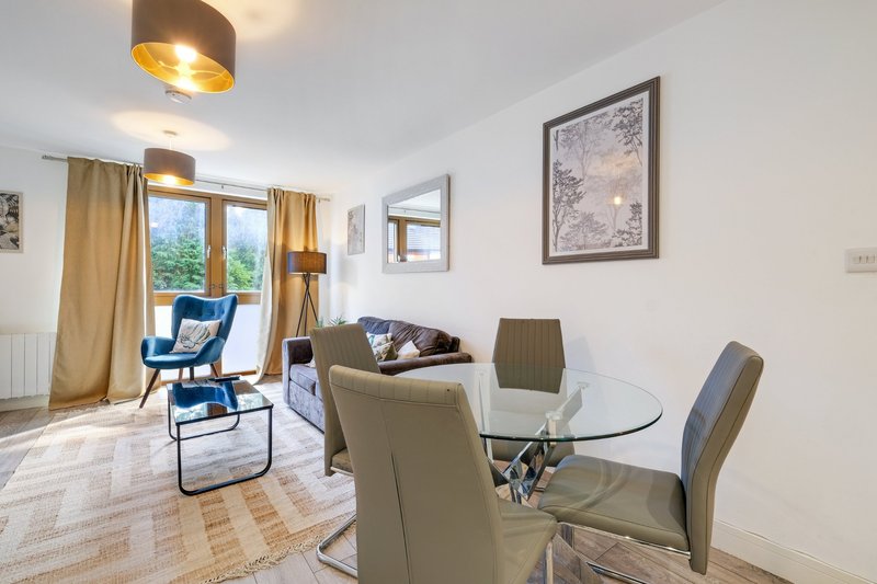 Modern living and dining area with glass table, upholstered chairs, and garden view through large windows