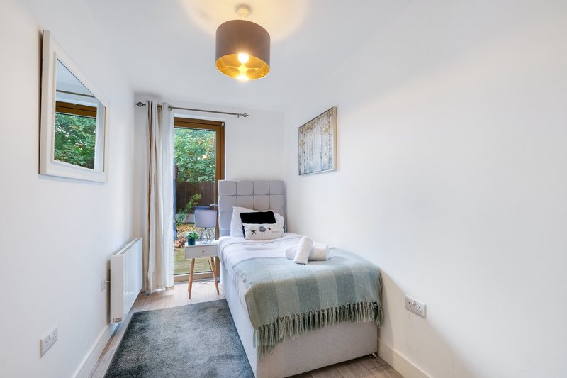 Bright bedroom with single bed, pendant light, windows, and access to garden area