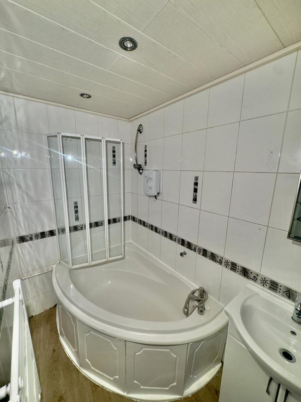 Modern bathroom with corner bathtub, glass shower enclosure, white tile walls and recessed ceiling lights
