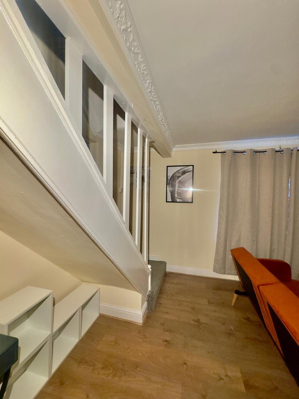 Hallway with wooden stairs, cream walls, framed artwork, and orange bench seating