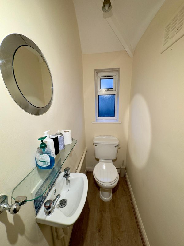 Compact bathroom with round mirror, wall-mounted sink, toilet, and small window