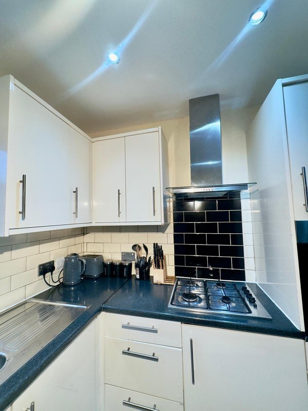 Modern kitchen with white cabinetry, black countertop, gas hob, and subway tile backsplash