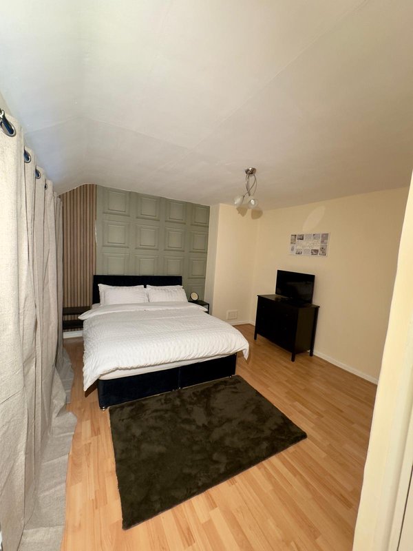 Bedroom with double bed, wooden floor, dark rug, and wall-mounted TV