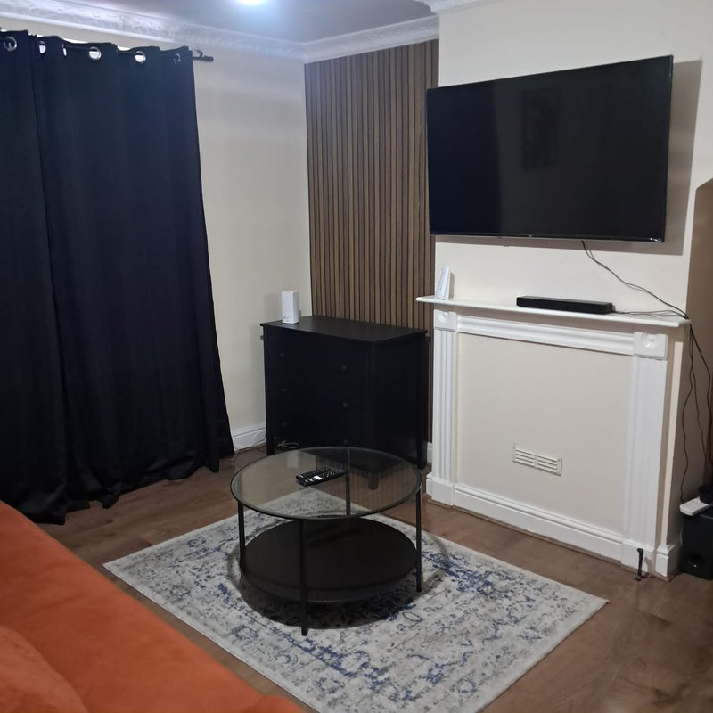 Living room with wall-mounted TV, black round coffee table, white fireplace and dark curtains