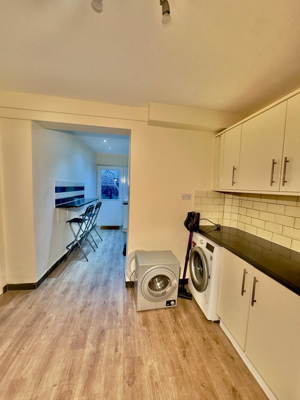 Laundry room with washing machine, white cabinetry, and view to living area