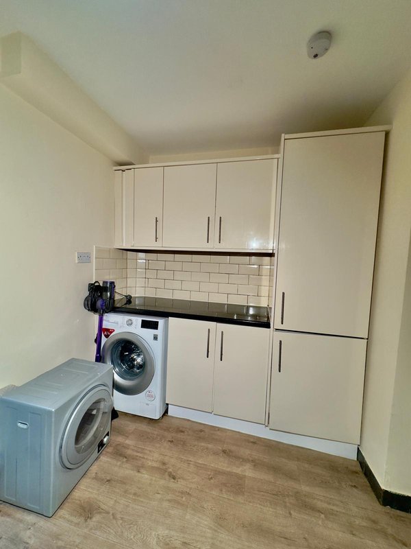 Laundry room with two washing machines, white cabinetry, and wooden flooring
