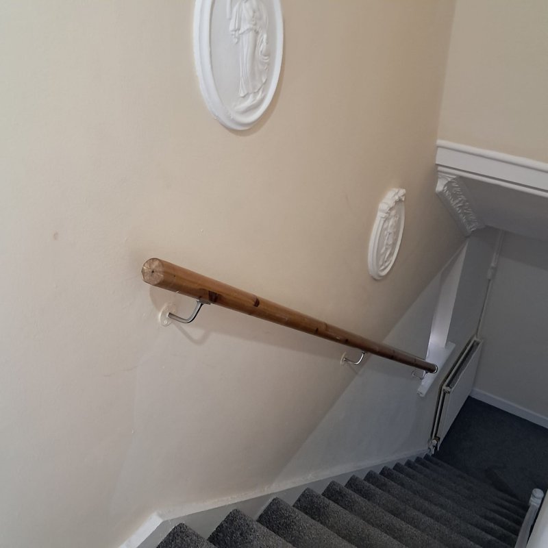Stairwell with wooden handrail, white wall medallions, and gray carpeted steps