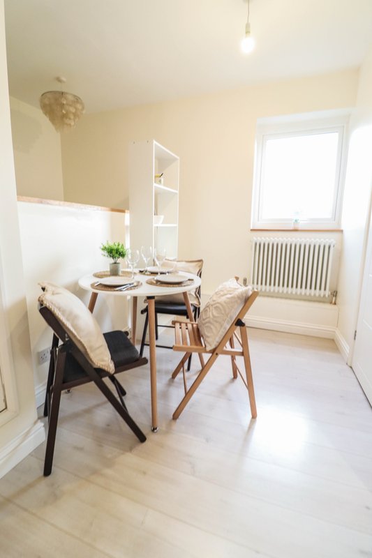 Bright dining area with wooden table, two chairs, shelving unit and window