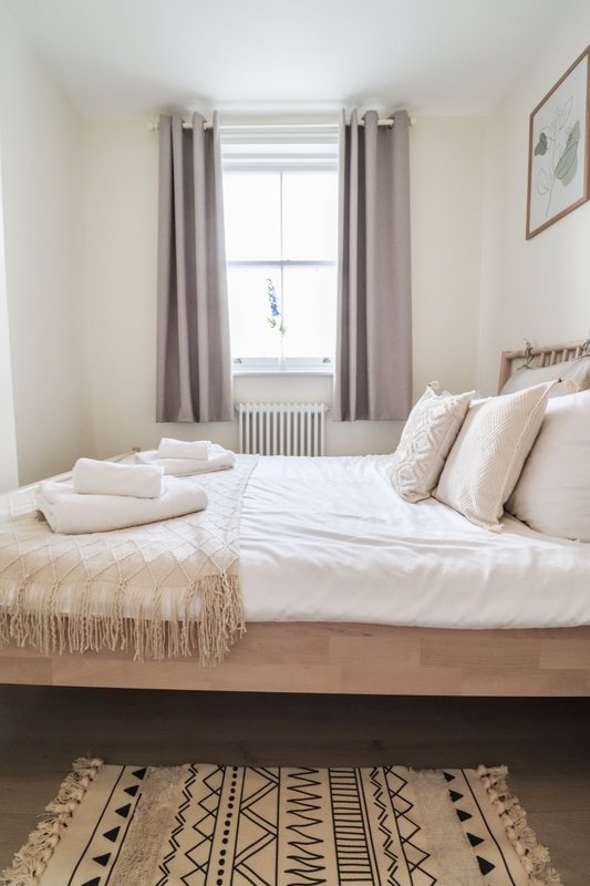 Bright bedroom with double bed, white bedding, grey curtains and geometric patterned rug