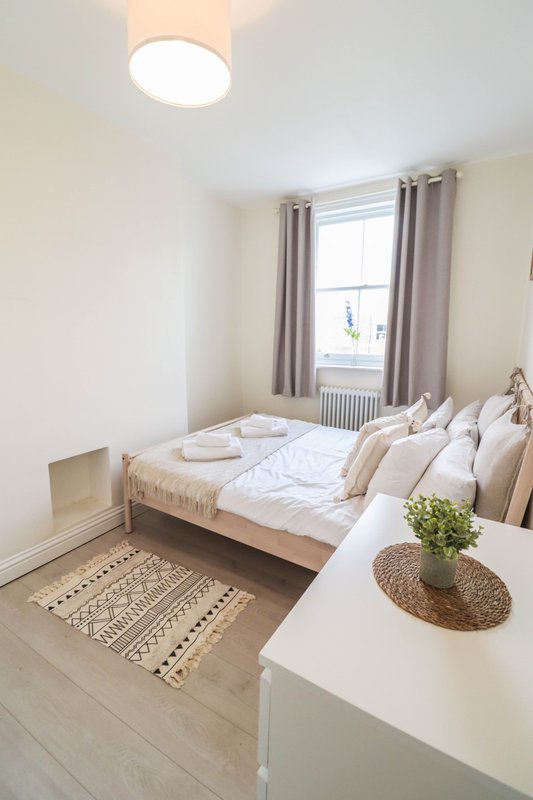 Bright bedroom with double bed, white bedding, cushions, wooden floor and potted plant