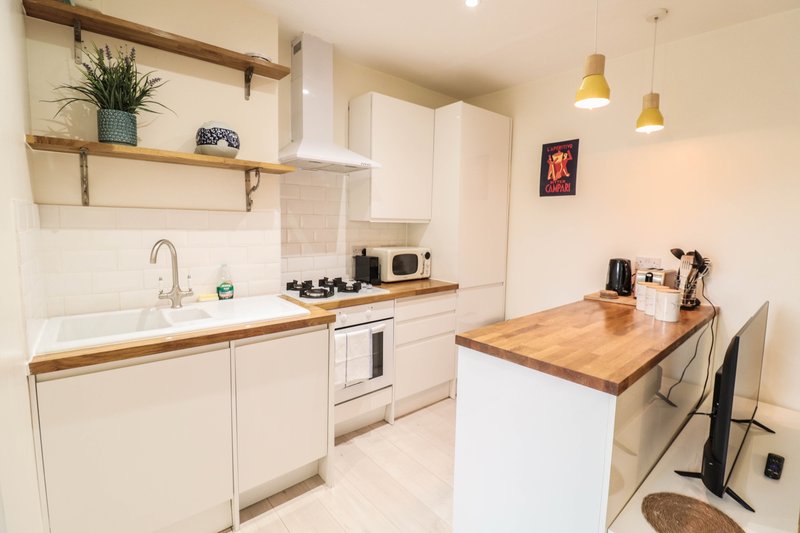 Modern white kitchen with wooden countertops, island, gas hob, and open shelving with decor