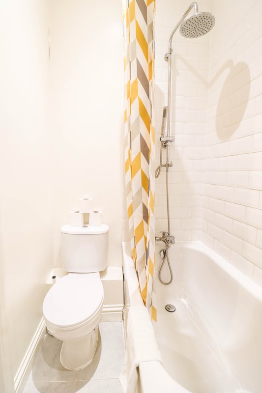 Compact bathroom with white toilet, shower with yellow patterned curtain and rainfall showerhead