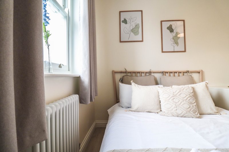 Bright bedroom with double bed, wooden headboard, white bedding, and framed botanical prints