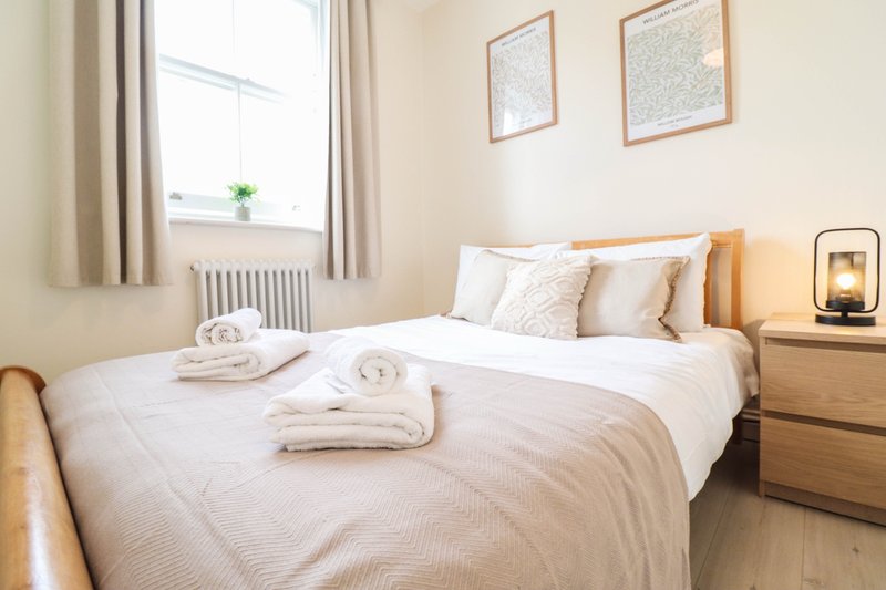 Bright bedroom with double bed, wooden headboard, bedside lamp and framed wall art