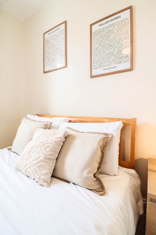 Bright bedroom with wooden bed frame, white bedding, patterned cushions and framed wall art