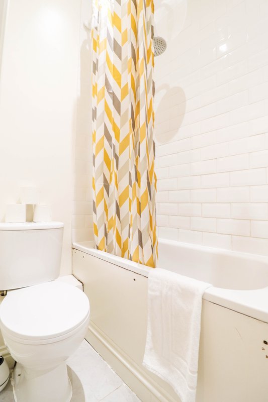 Clean bathroom with white toilet, bathtub, yellow geometric shower curtain and towel rail