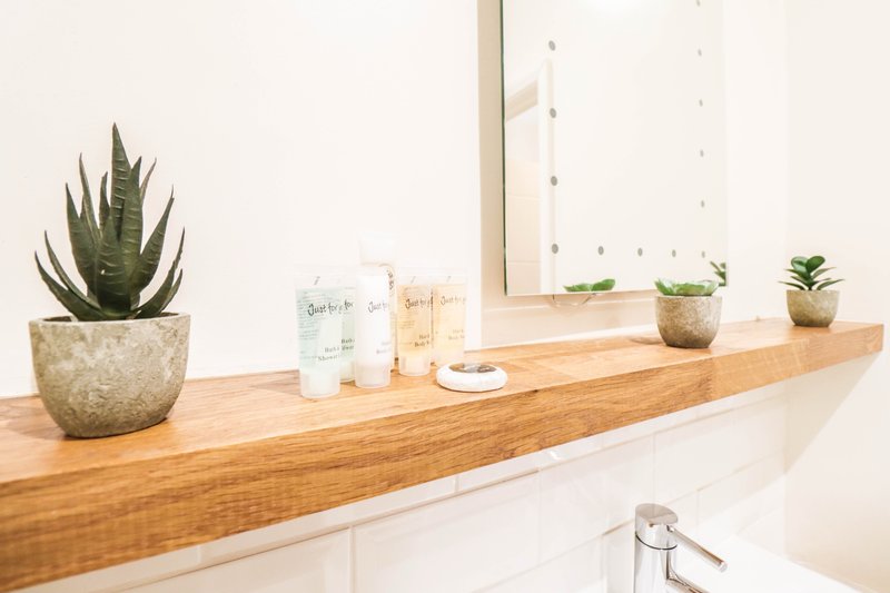 Bathroom sink counter with wooden shelf, potted succulents, toiletries and mirror