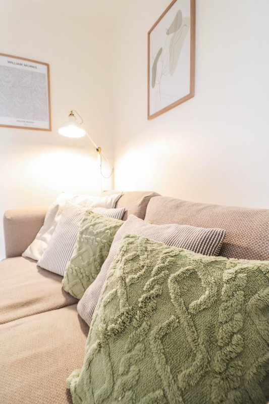 Bedroom with beige sofa, green quilted throw, striped and white pillows, wall art and pendant lamp