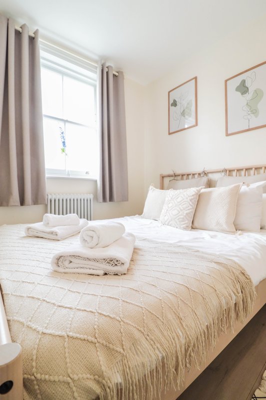 Bright bedroom with double bed, cream bedding, rolled towels, and framed botanical prints