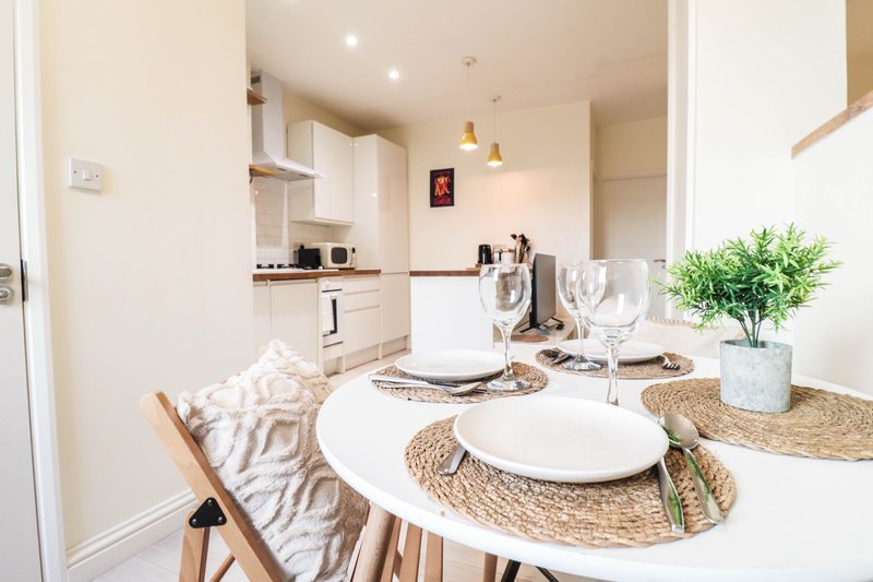 Open-plan kitchen and dining area with white cabinetry, round table, place settings and fresh flowers