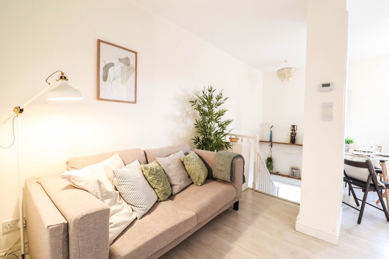 Bright living room with beige sofa, scatter cushions, arc lamp, framed artwork, and potted plant
