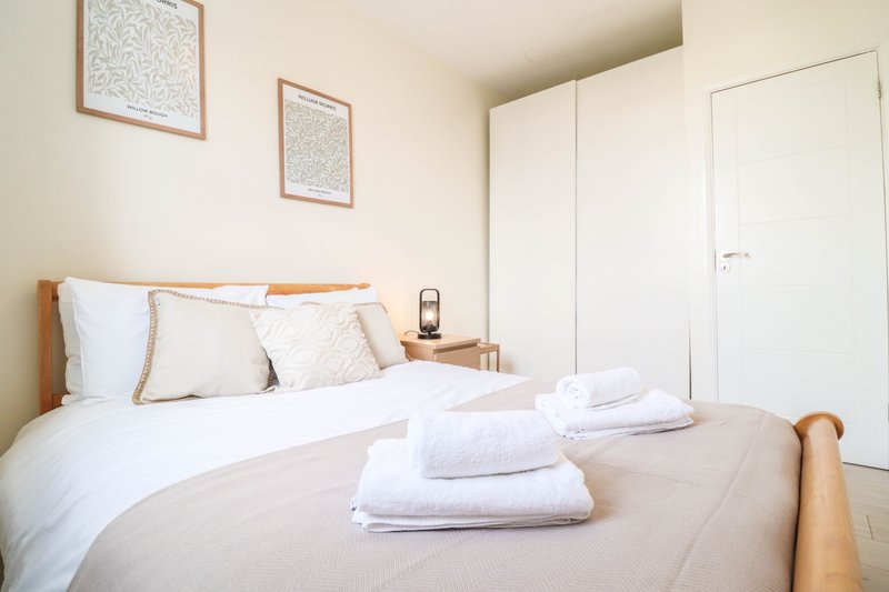 Bright bedroom with double bed, white bedding, wooden headboard and wardrobe