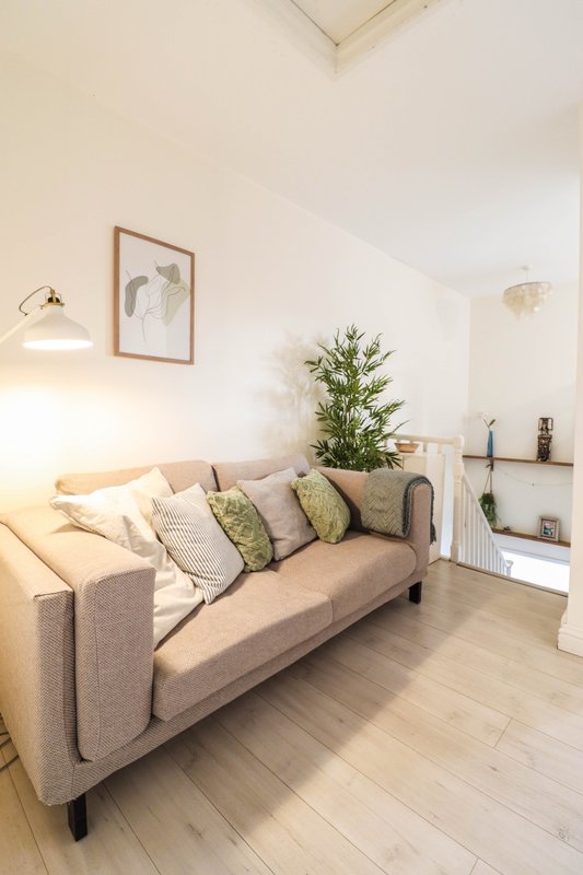 Bright living room with beige sofa, cushions, potted plant, framed artwork and wooden flooring