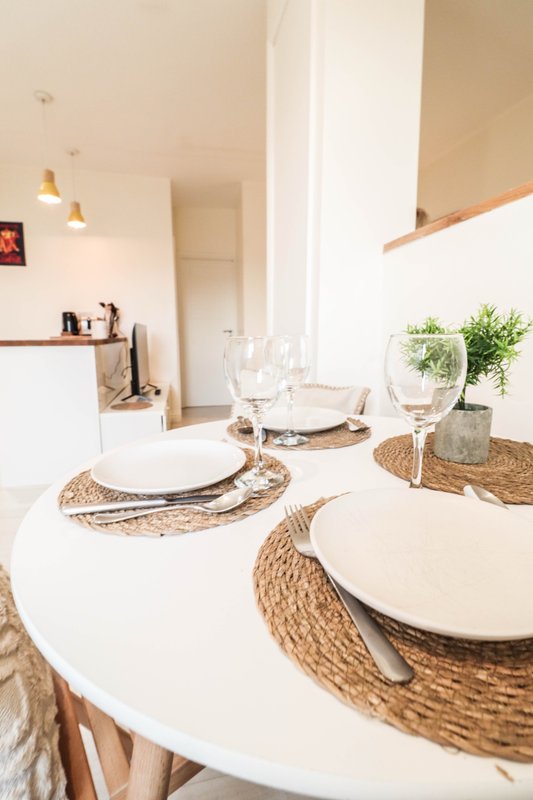Modern dining area with round white table, place settings, woven placemats and fresh potted plants