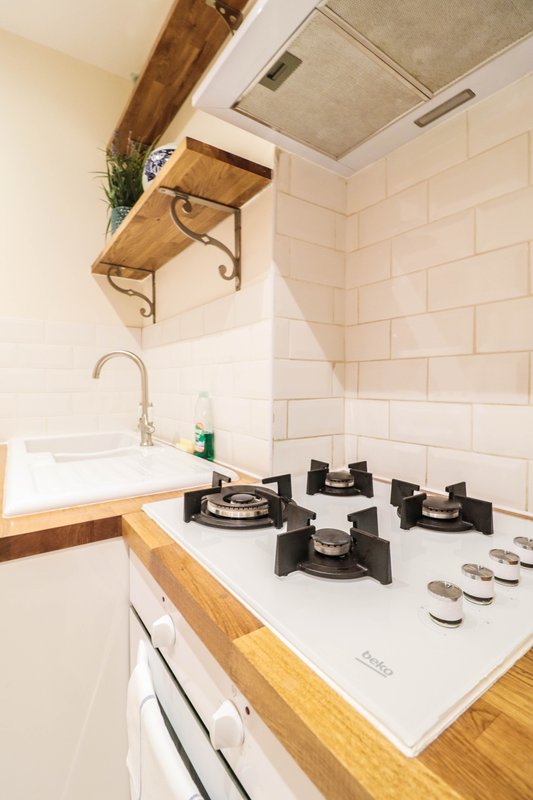 Kitchen with gas hob, white subway tiles, wooden shelf and chrome tap