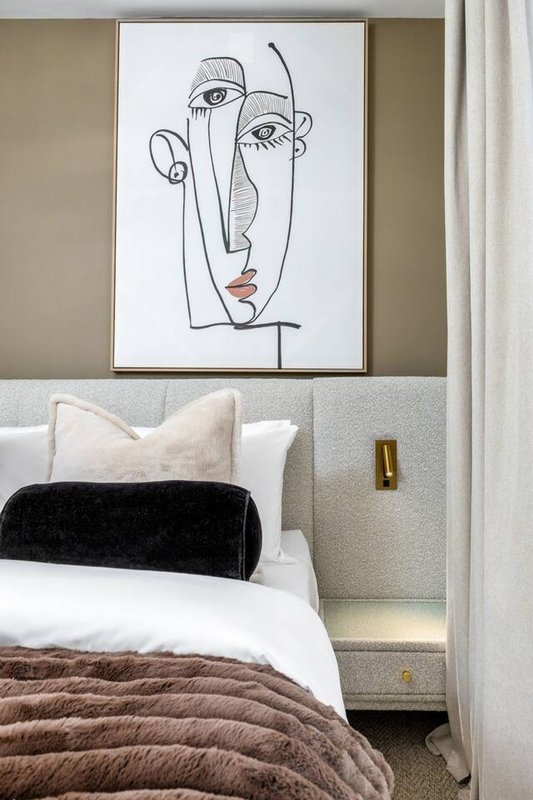 Bedroom with double bed, abstract line-art portrait above headboard, black cushion and white pillows