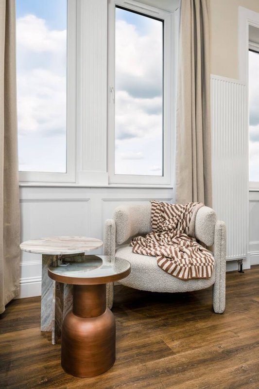 Bright window seat with upholstered armchair, geometric throw blanket, and round side tables