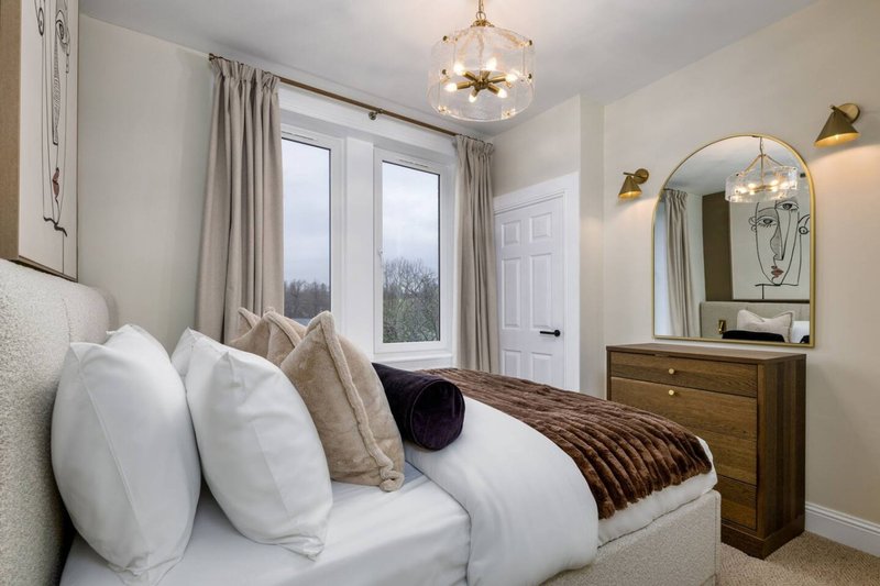 Bright bedroom with double bed, white pillows, wooden dresser and arched mirror