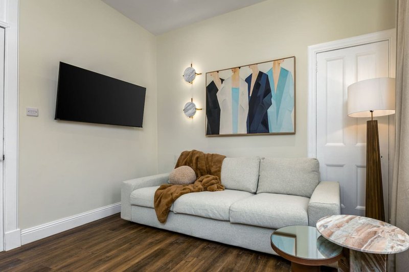 Living room with grey sofa, wall-mounted TV, abstract wall art, wooden floor and table lamp