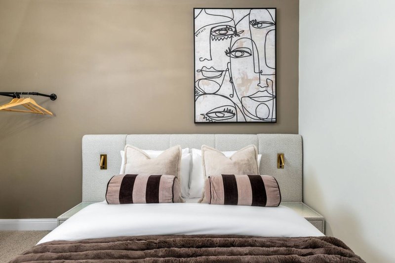 Modern bedroom with upholstered headboard, striped pillows, and abstract line art wall print