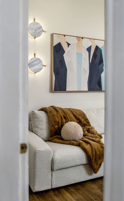 Modern bedroom alcove with upholstered armchair, mustard throw, wall sconces and abstract artwork