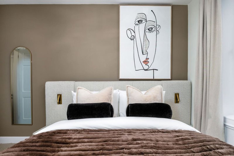 Modern bedroom with grey upholstered bed, black pillows, brown throw, and abstract line art above headboard
