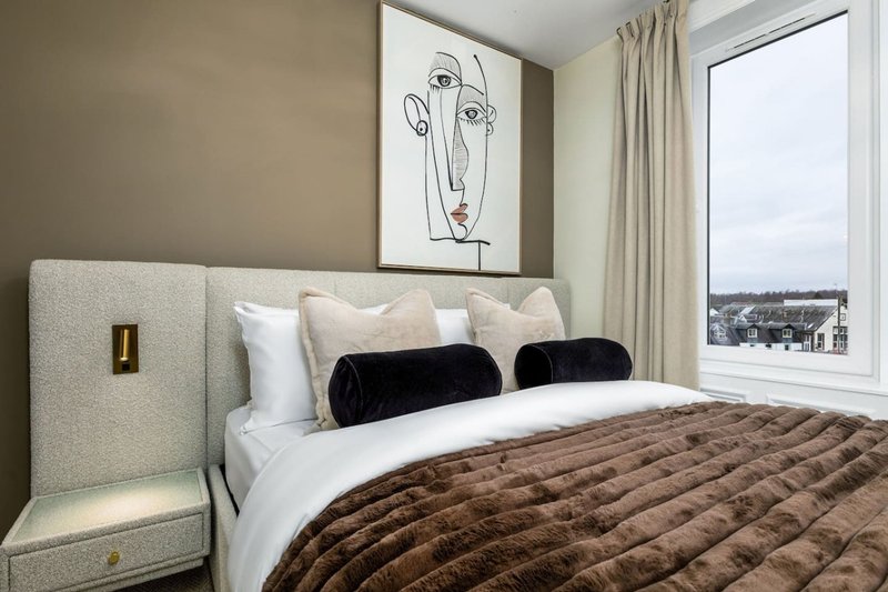 Modern bedroom with upholstered headboard, quilted brown bedding, black cushions and city view window
