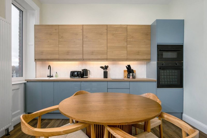 Modern kitchen with blue and wood cabinetry, round wooden dining table and chairs in foreground