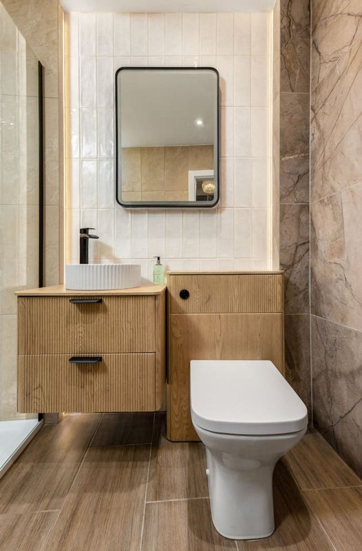 Modern bathroom with wooden vanity, white sink, framed mirror, and toilet