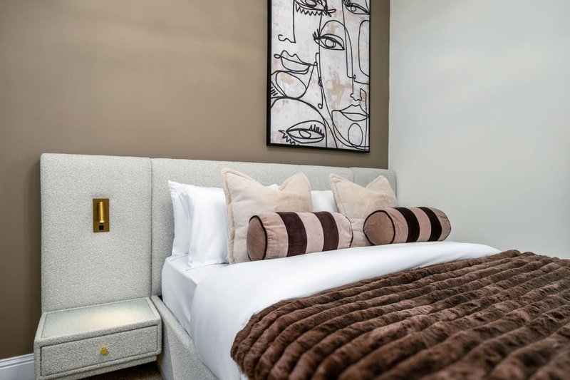 Modern bedroom with upholstered headboard, striped decorative pillows, brown quilted bedcover and wall art