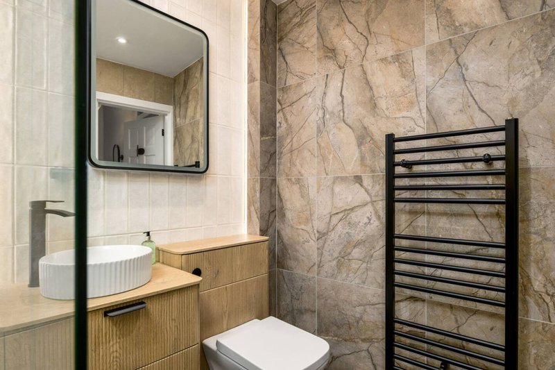 Modern bathroom with wooden vanity, mirror, toilet, and heated towel rail
